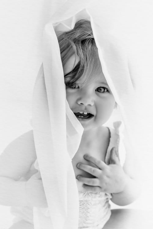 Toddler peeking out from behind a white muslin cloth