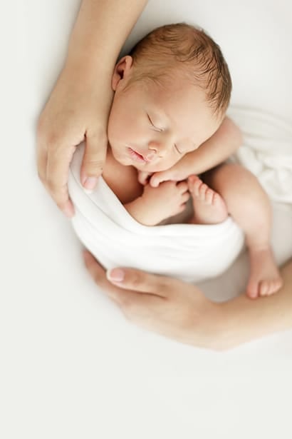 Newborn baby asleep in a white wrap, held in his mother's hands