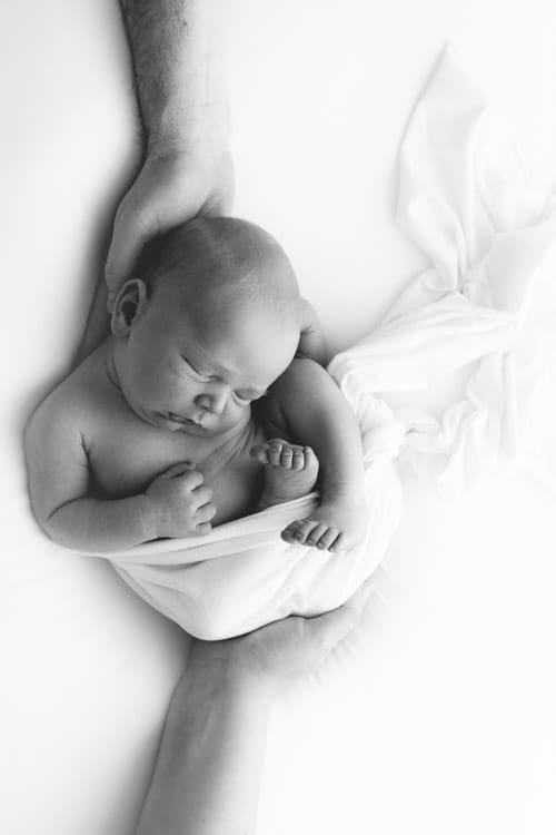 Newborn baby wrapped in white, cradled in a parent's hands