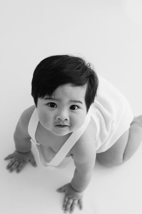 Baby on hands and knees on a white backdrop, looking at the camera
