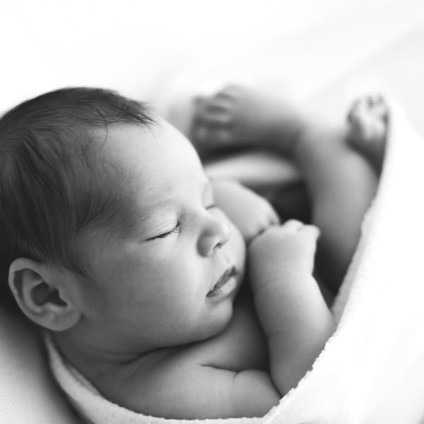 Newborn asleep on a soft white blanket with both hands tucked under the chin