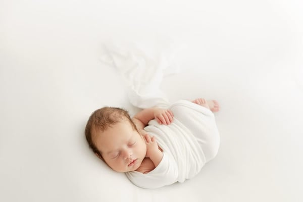 Newborn asleep, swaddled in a soft white wrap