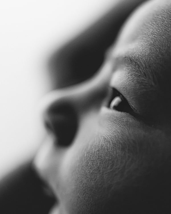 A parent and newborn cheek to cheek in low light, in black and white