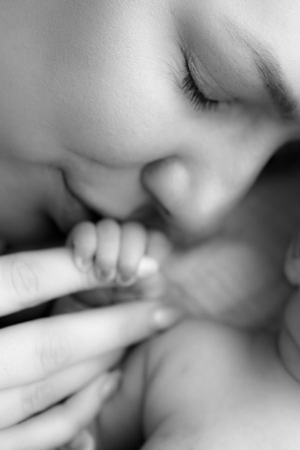 A newborn's hand curled around an adult finger, close to the mother's face, in black and white