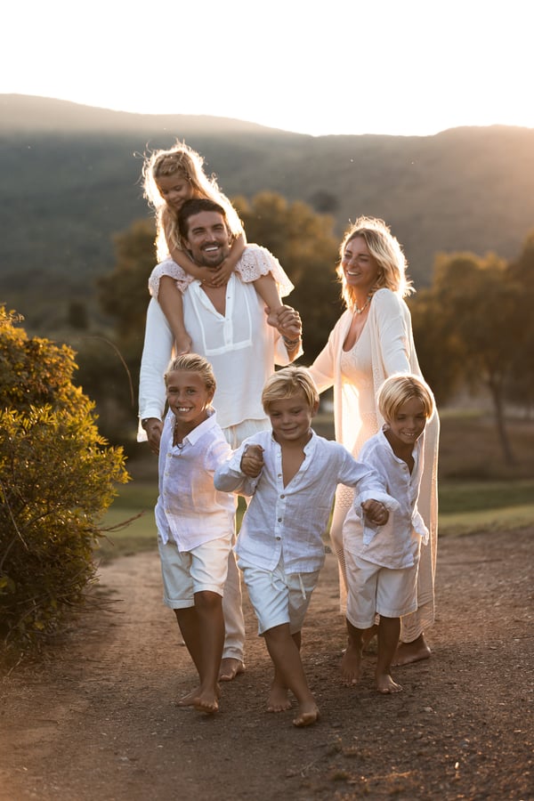 A family walking along a path at golden hour, one child up on their father's shoulders, hills behind them