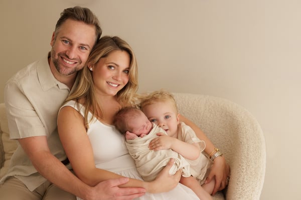 Both parents, the big brother and the newborn together, all looking at the camera