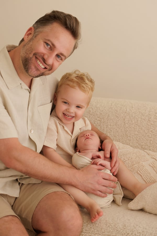 A father seated with the big brother on his knee and the newborn in his arms