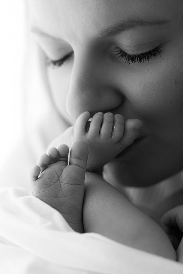 A mother holding her newborn's foot to her lips, in black and white