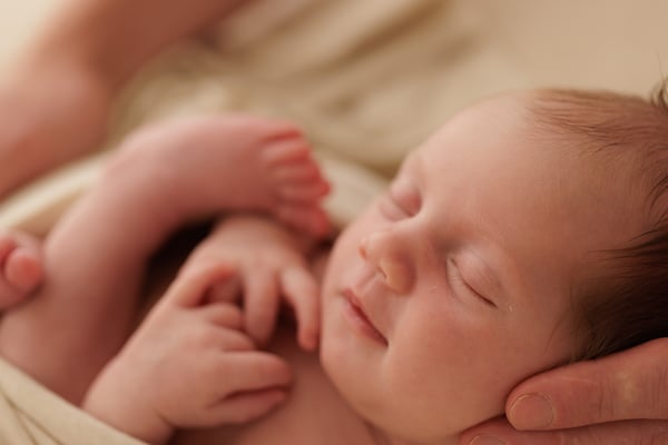 A newborn asleep with both feet resting in an adult hand