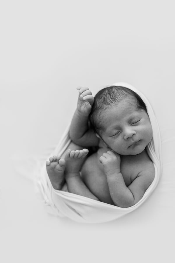 A newborn asleep in a loose white wrap, arms and legs free, seen from above
