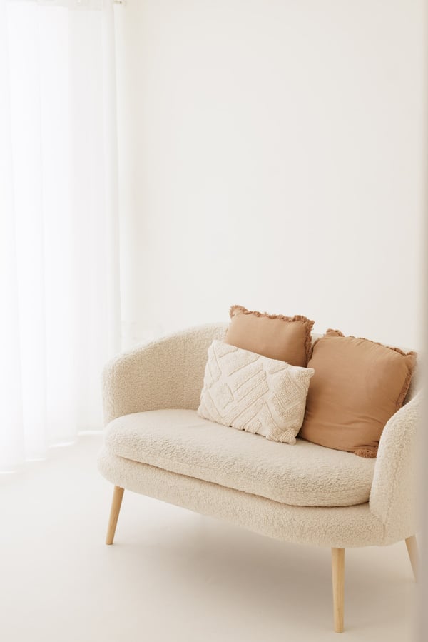 A cream boucle sofa with soft cushions, beside the voile curtains