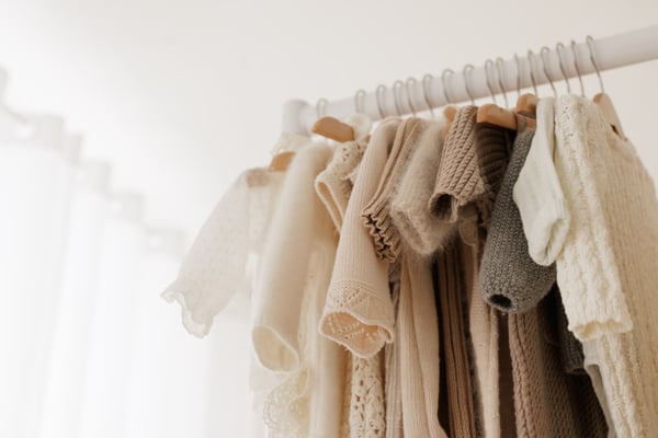 A rail of small knitted outfits hanging against the voile curtain