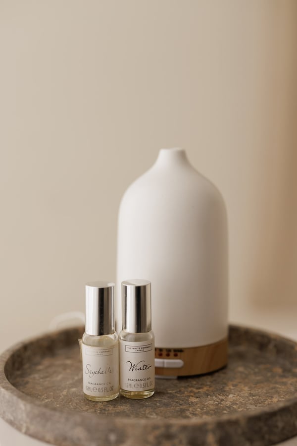 The diffuser and two spray bottles standing on a stone tray against a warm wall