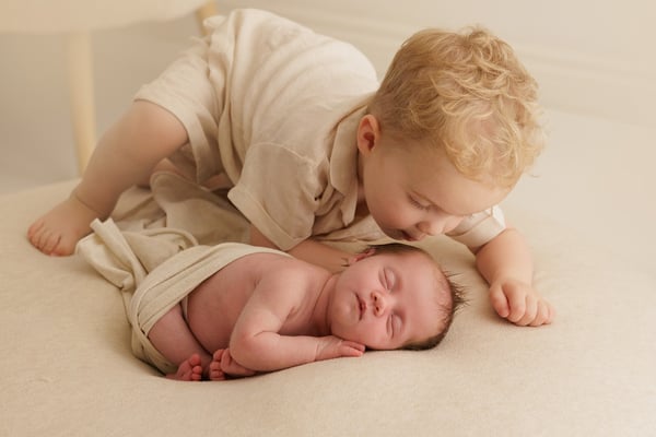 A big brother kneeling down to kiss his sleeping newborn sister