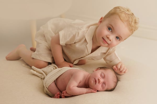 A big brother looking at the camera from beside his sleeping newborn sister