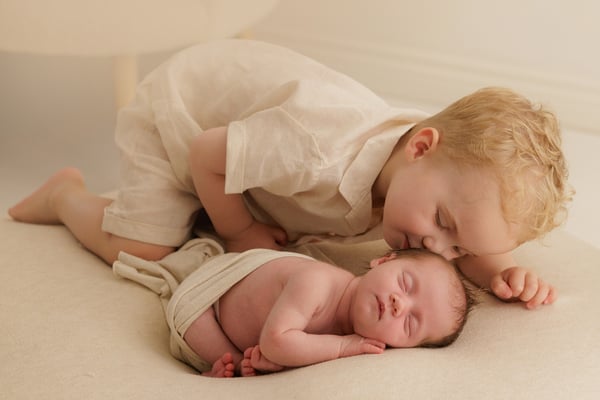 A big brother lying down beside his newborn sister and kissing her