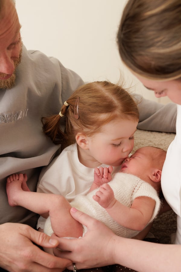 A big sister kissing the newborn, who is held in her parents' arms between them
