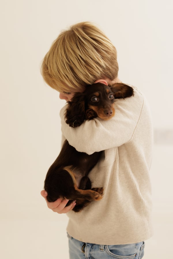 A child holding the family's dachshund in both arms in the studio