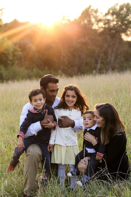 A family of five walking together in a field with the sun low behind them