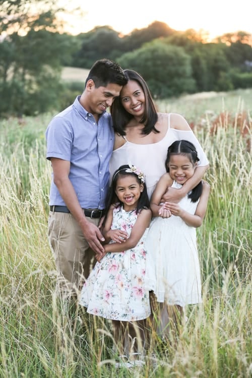 A family of four standing together in long grass at the edge of a wood