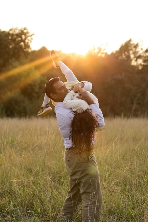 A mother lifting her baby up against the setting sun in an open field