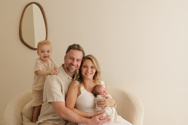 Both parents seated in an armchair with the newborn and the big brother beside them