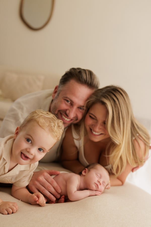 Both parents and the big brother around the newborn, the brother laughing at the camera