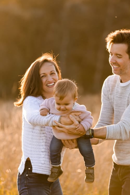 Parents holding their baby between them in a field at golden hour