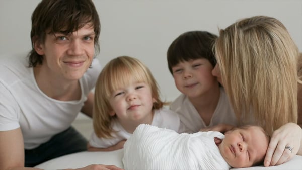 Parents and two young children gathered around a swaddled newborn on a white bed