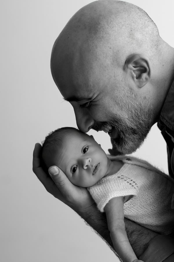 A father holding his newborn in both hands, the baby awake and looking up, in black and white