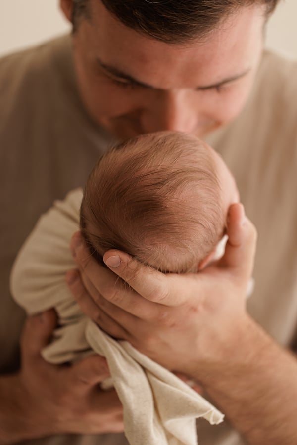 A father holding his newborn against his chest, his face lowered to the baby's head