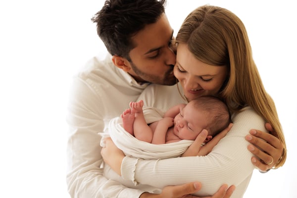 A father kissing the mother's head while she holds their newborn between them