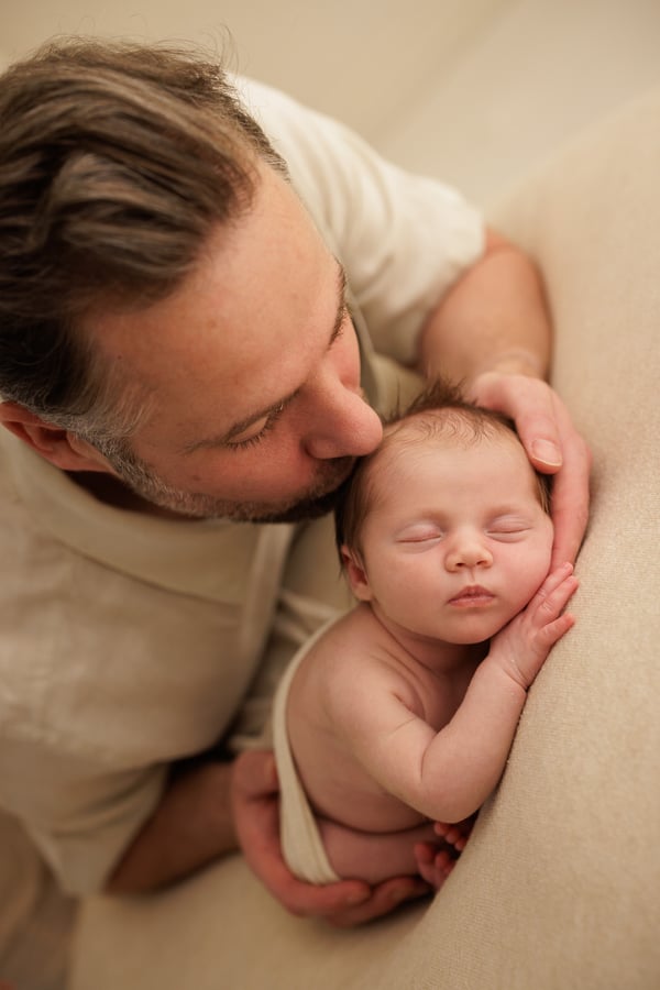 A father holding his newborn in both arms and kissing her head