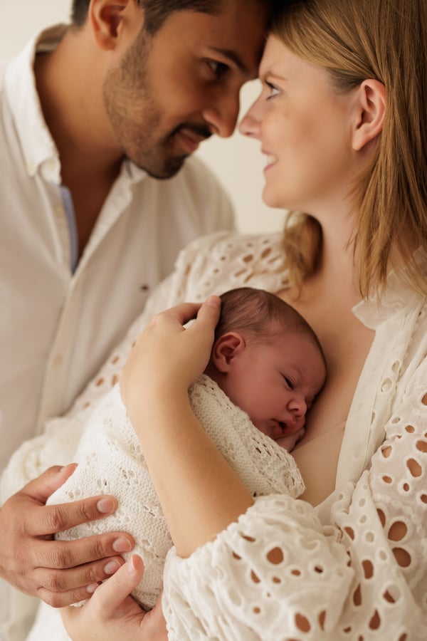 A father looking at the mother as she holds their newborn against her
