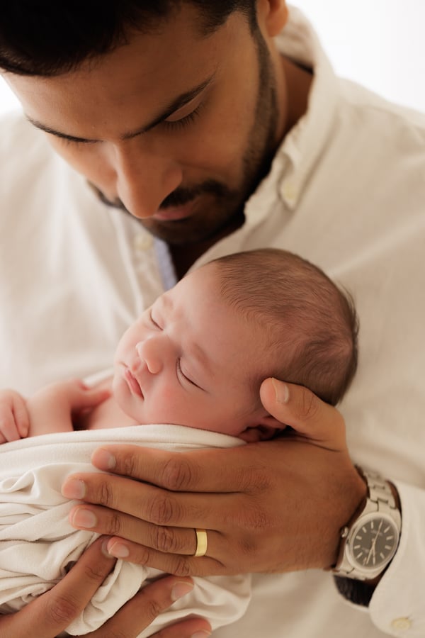A father holding his swaddled newborn against his chest and looking down at them