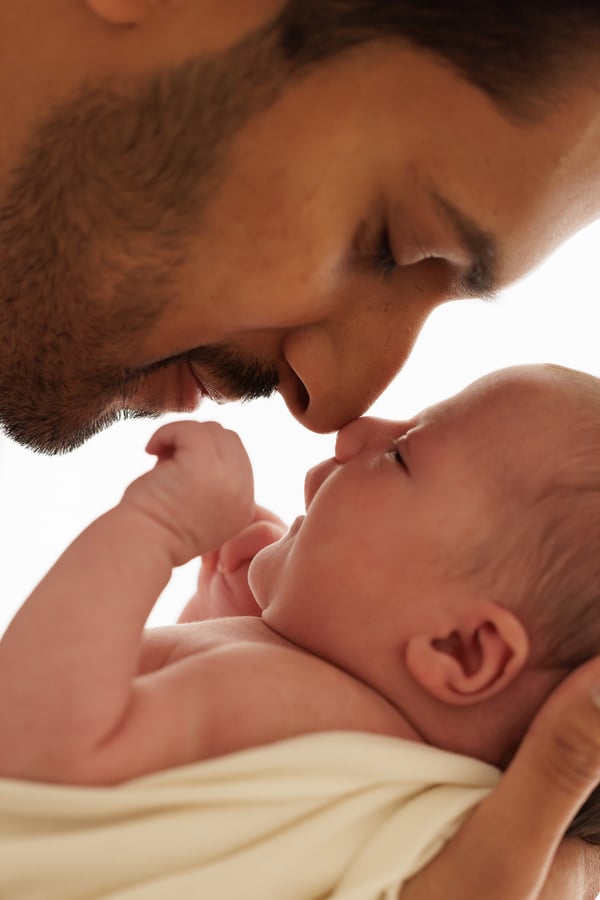 A father leaning nose to nose with his newborn, the baby awake in his arms