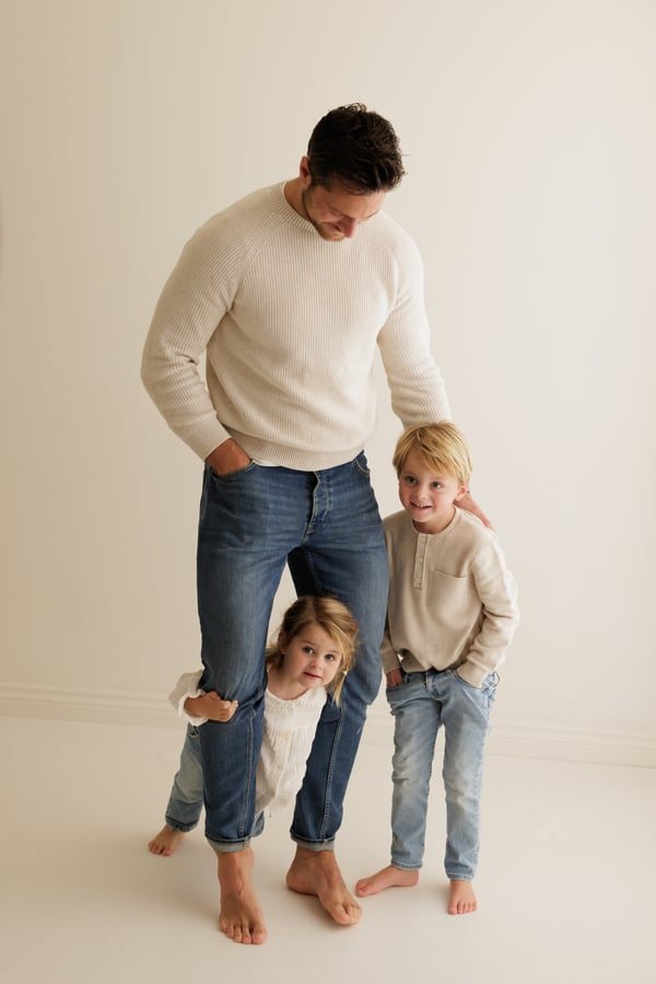 A father standing in the studio with his three children gathered around his legs