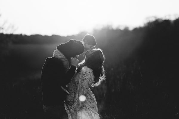 A couple kissing in a field at sunset, strongly backlit, in black and white