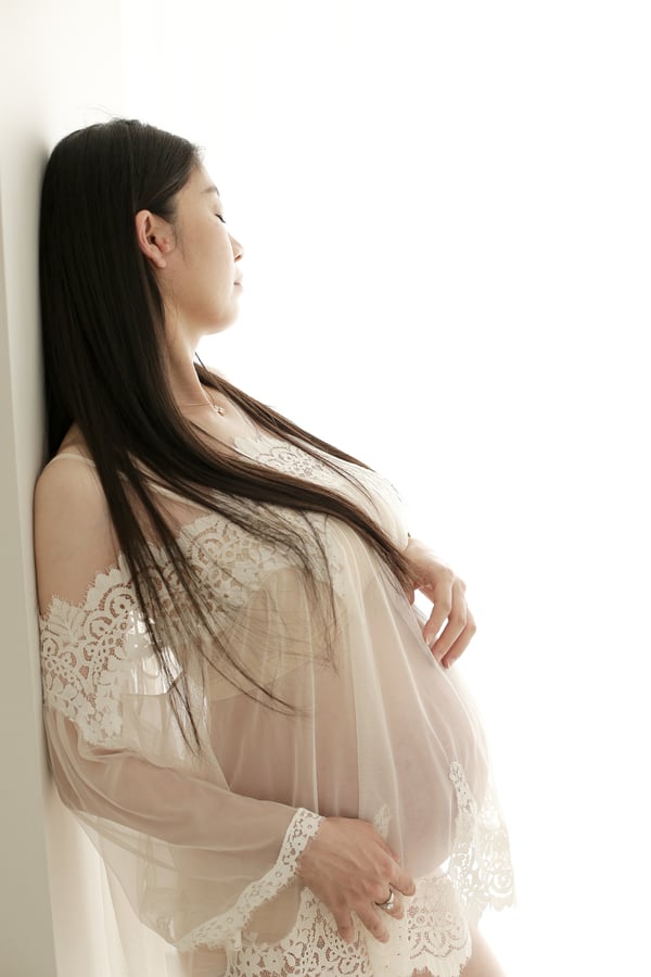 An expectant mother in a cream lace robe standing in profile, hands resting on her bump