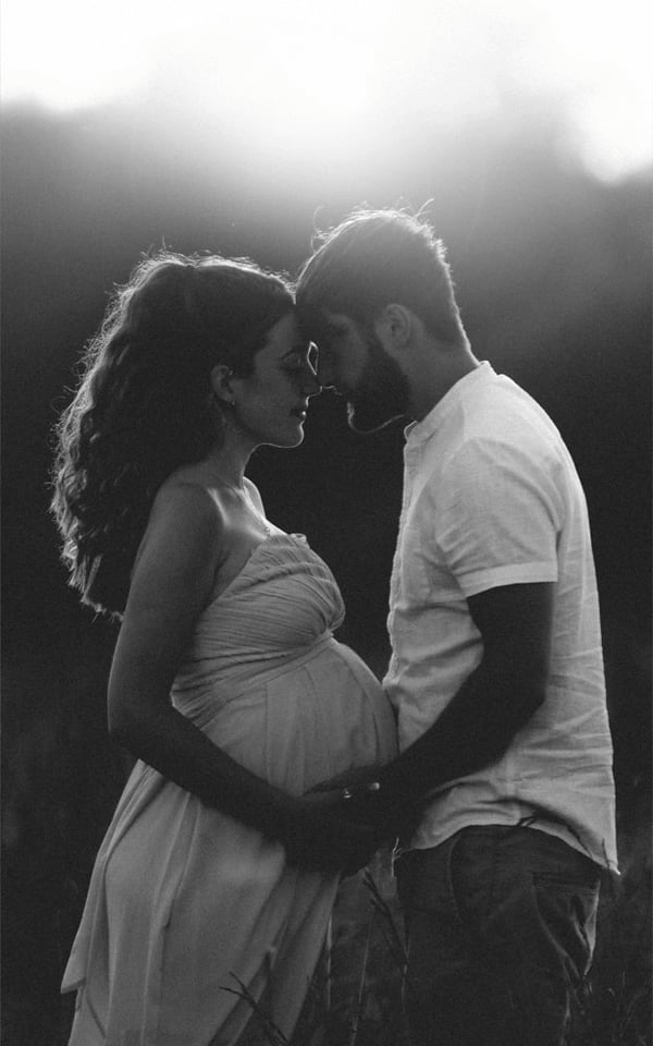 Expectant couple standing forehead to forehead in a field at dusk