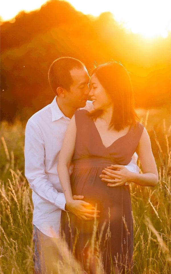 Expectant couple in tall summer grass, backlit by golden evening light