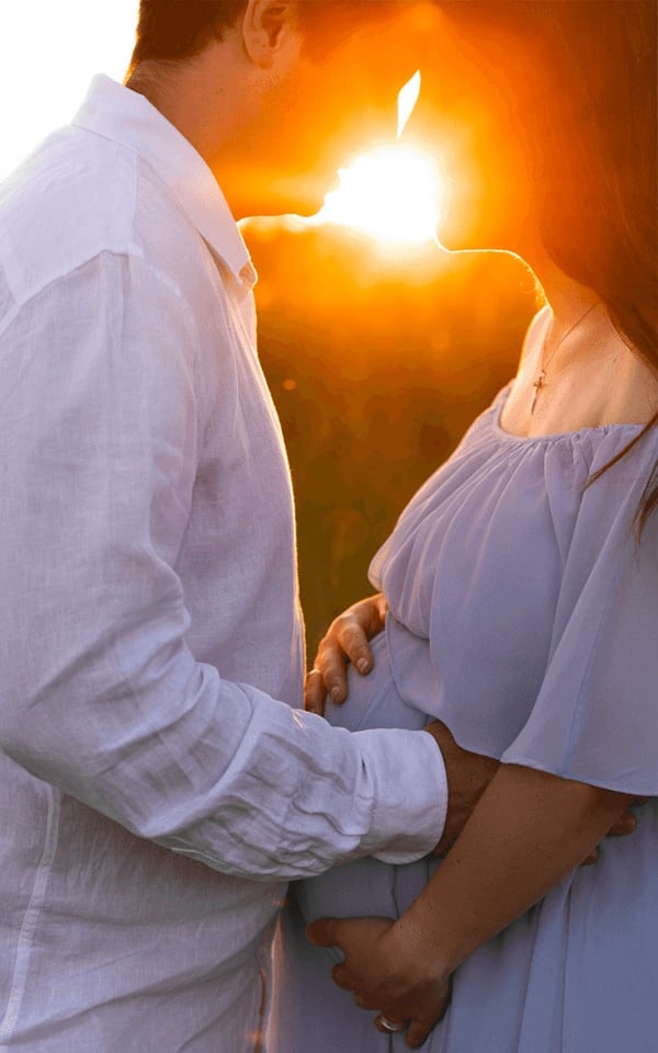 Expectant couple embracing at sunset, the low sun flaring between them