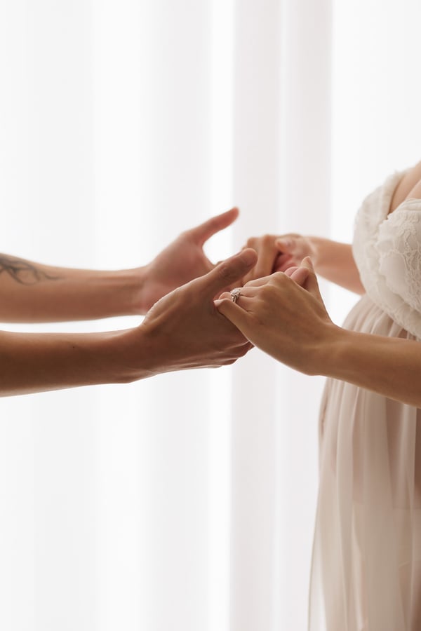 Two pairs of hands held together against a bright background, a ring visible