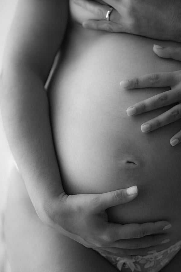 Close-up of two pairs of hands resting on a bare pregnant belly, in black and white