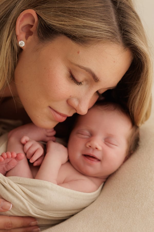 A mother lying cheek to cheek with her swaddled newborn