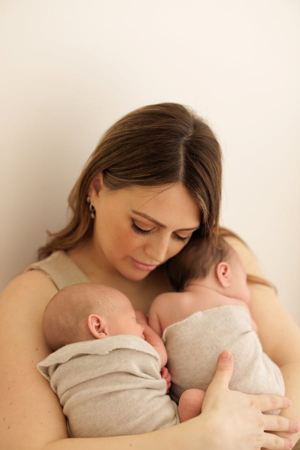 A mother holding her twin newborns, one wrapped in each arm