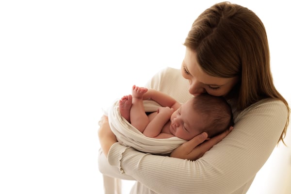 A mother holding her swaddled newborn against her shoulder and looking down at them