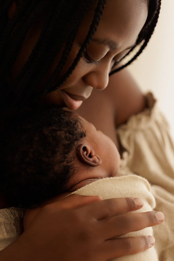 A mother holding her newborn against her shoulder and looking down at them