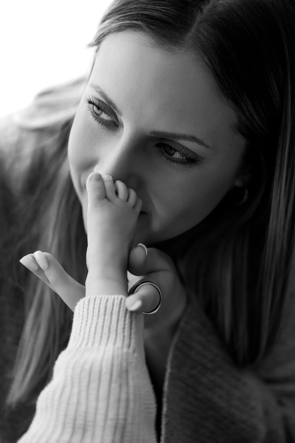 A mother holding her baby's foot to her lips and kissing it, in black and white