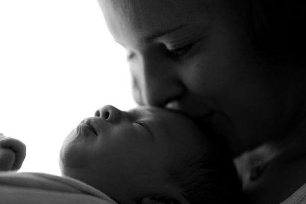 A mother kissing her newborn in low light, in black and white